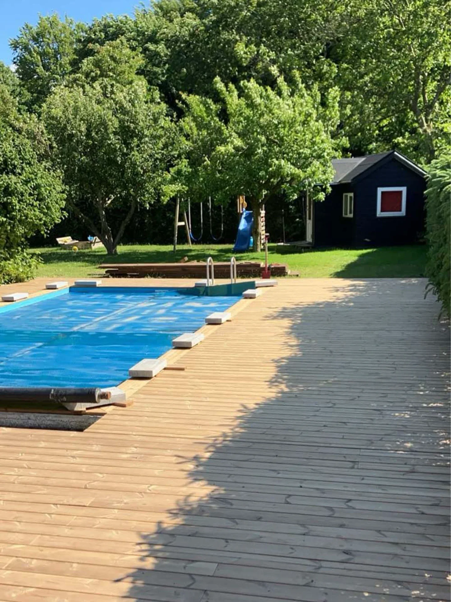 Udendørs swimmingpool med trædæk og grønne træer i baggrunden.