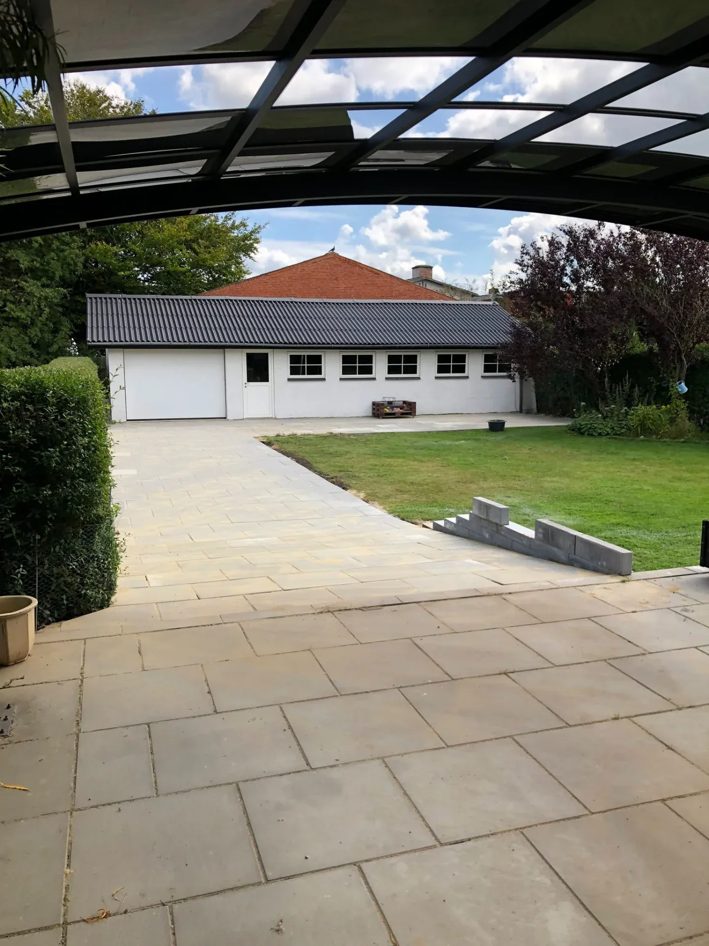 Udendørs terrasse med glasoverdækning og velplejet have.